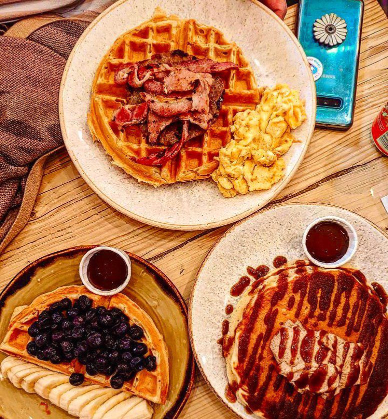 A colourful brunch table at The Cabin in Sheffield featuring fluffy pancakes, crispy waffles, fresh berries, vegan chicken, and creamy lattes—one of the most popular brunch spots in Sheffield.