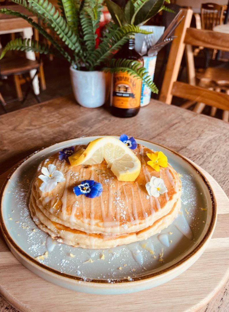 Stack of fluffy pancakes topped with lemon and edible flowers
